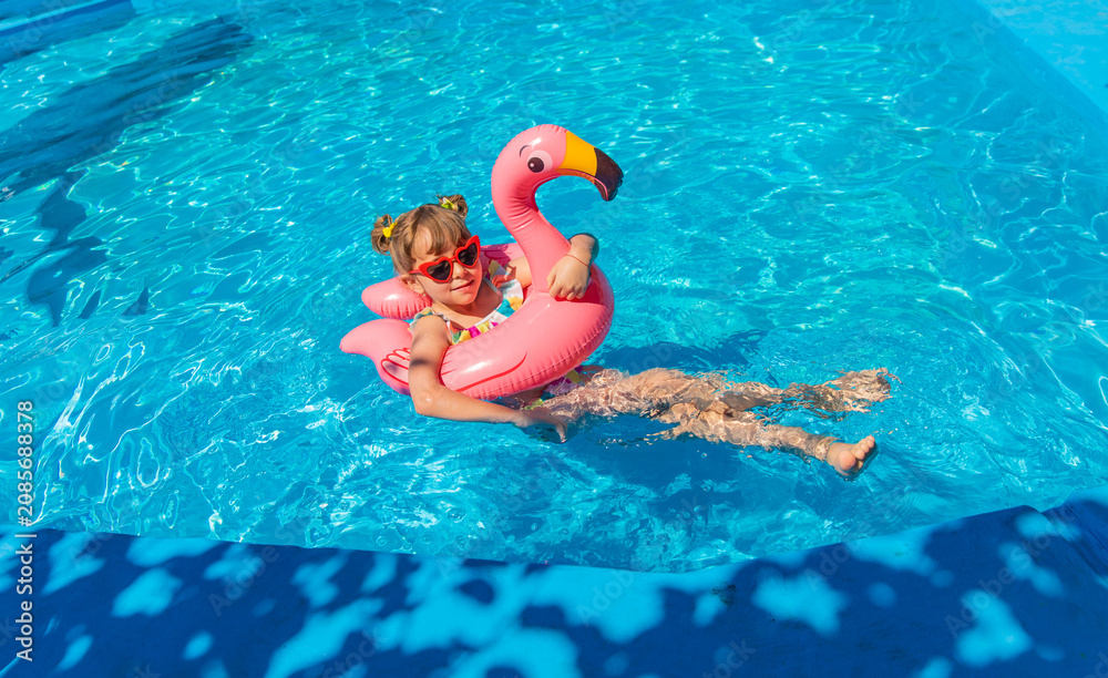 Naklejka premium A child swims in a pool surrounded by flamingos. Selective focus.