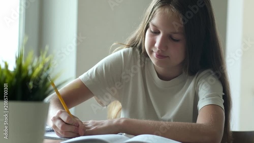 Smiling young girl writing in notebook with yellow pencil during home studies. Concept of education and homework