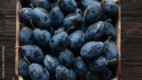 Fresh ripe blue plums in wooden crate close up top view