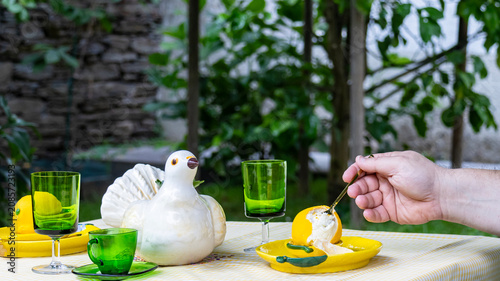 Tableau sur toile Hand taking a spoonful of a gourmet lemon-shaped dessert on a garden table