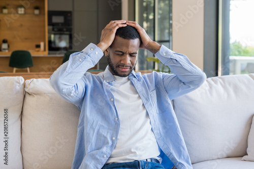 Foto Young man experiencing severe headache and discomfort while sitting on a comfort