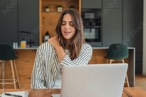 Foto Young woman experiencing discomfort and pain in her shoulder while working on a