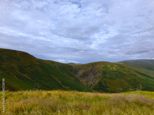 The beautiful historic geographic hollow and hill of the devil's beef tub, white cloud sky, with yellow grass in front of the view of Scotland