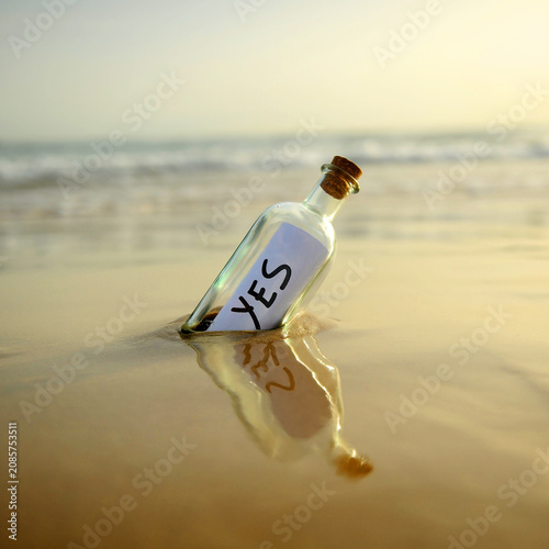 Yes message in a bottle at sunset. Bottle on the beach, washed ashore by the tide, affirmative answer sent. Affirmative response. Background of a misty beach with gentle waves in a square format.