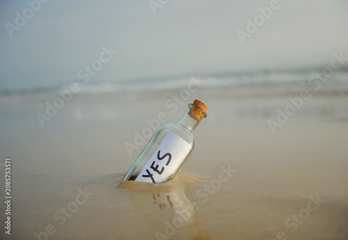 Bottle on the beach with an affirmative answer inside, yes, positive message. Affirmative response sent. Misty beach landscape background with gentle waves