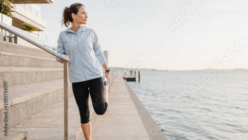 Sport luxe woman stretching beside modern waterfront steps