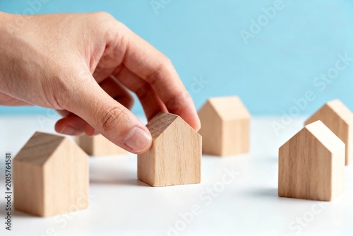 Hand Arranging Wooden House Models on Blue Background