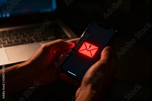Hands holding smartphone with red email alert in dark setting