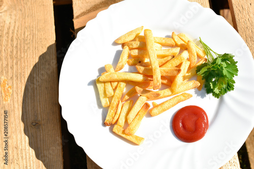 French fries with some ketchup and parsley on white plate on wooden background