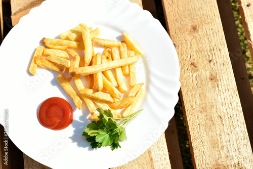 French fries with some ketchup and parsley on white plate on wooden background
