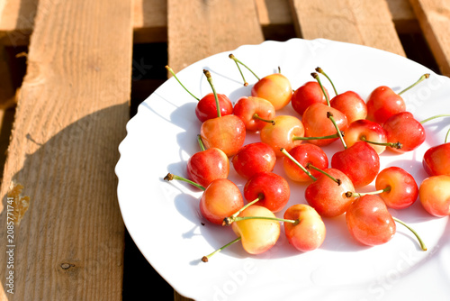 Ripe merry on white plate on wooden background, summer harvest 