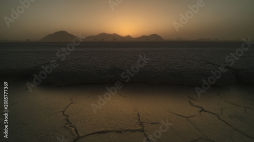 Sunset mountain silhouette over cracked desert mud with warm glow and moody sky