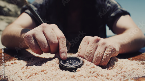Young person compass buried in sand on beach, hands exploring directional instrument with curious mood