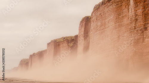 Soft sea mist along towering red cliff face at coastal shoreline creating moody atmosphere