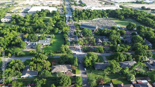 Crowds gather across Farmers Branch Historical Park green lawns during July Fourth Independence Day festivities. Sprawling oak trees shade expansive historic grounds throughout suburbs Dallas, TX