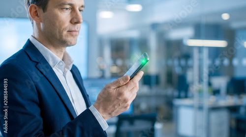 Professional man holding a smartphone with a glowing green light on the screen in a modern office environment smartphone business technology internet