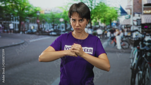 Bilde på lerret Volunteer woman, young with short hair, scowling while pressing fist to open palm beside parked bicycles on a busy street, wearing a purple volunteer t shirt; determination focus