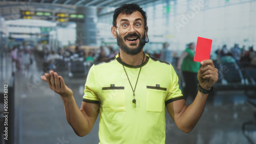Schilderij op canvas Referee man holds red card high and shows whistle necklace with palm up gesture in airport; discipline authority