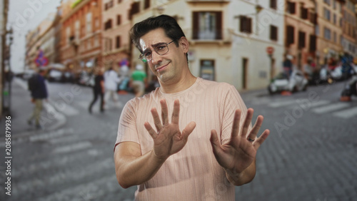 Fotografie Man pushes palms forward in stop gesture at crosswalk on cobblestone street; hesitation restraint caution