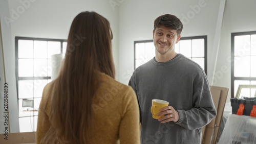 Foto Young man holding a yellow mug with both hands while receiving coffee from woman in building; moving together affection