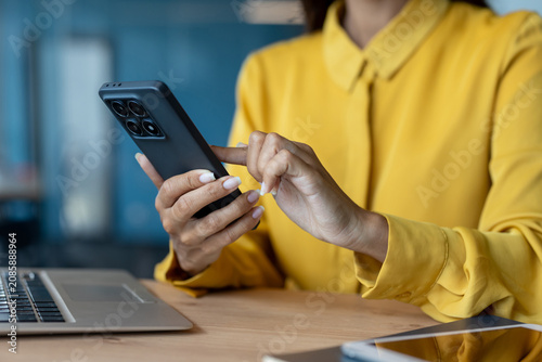 Close-up photo of female young hands in a yellow shirt wearing corsets and typing on a mobile phone