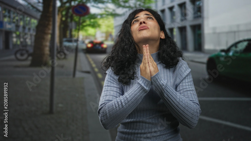 Foto Woman with hands clasped in prayer on a city street, eyes closed and tears on her cheeks, palms held near face in pleading gesture; pleading hope