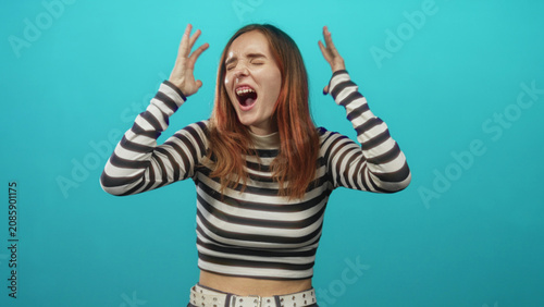 Quadro su tela Young redhead woman in black and white striped top clenches fists, grimaces and squeezes eyes shut while centered against a turquoise studio backdrop; frustration