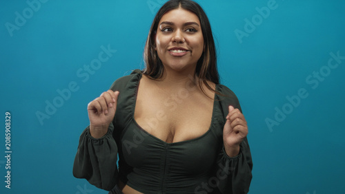 Canvas Print Woman showing visible cleavage with open hands and warm smile, speaking toward camera in studio, wearing green crop top; confidence warmth friendliness