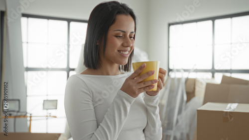 Photos Woman holding yellow mug smelling coffee inside a building amid moving boxes and packing supplies; contentment fresh start