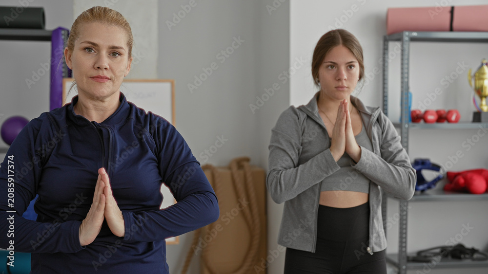 Obraz premium Woman with hands pressed together performing prayer gesture in fitness studio with mats and weights visible; mindfulness wellness family serenity.