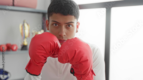 Fotografía Man throwing a jab with red boxing gloves in a training studio with trophies on shelf; determination