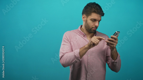 фотографія Man with beard tapping smartphone screen, finger on phone while looking down in studio; concentration productivity