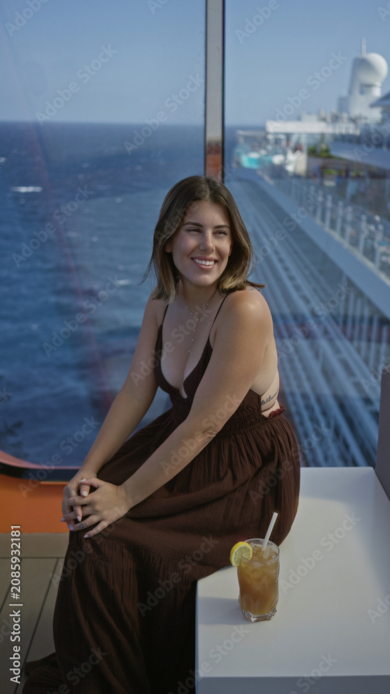 Fototapeta premium Woman smiling and sitting showing cleavage on cruise ship terrace with ocean view and drink nearby; relaxed serenity.