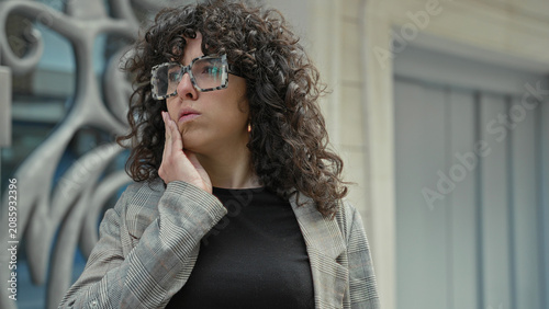 Фотография Young woman touching cheek with hand by a building entrance and ornate metal gate; pensive introspection