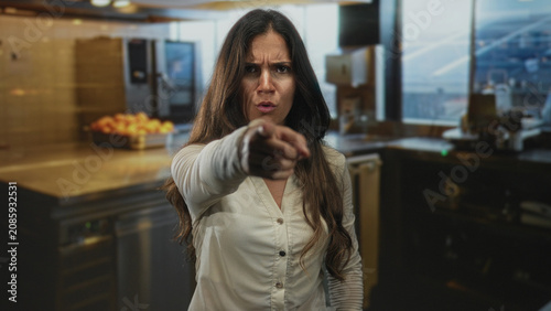 Foto Woman points finger to camera in kitchen while frowning with extended hand visible; confrontation anger demand