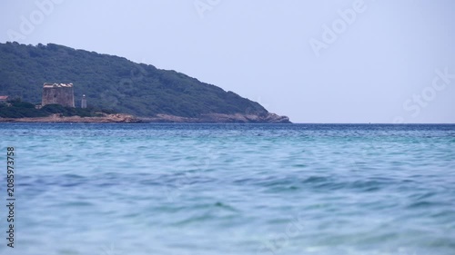 Scenic view of Sardinia’s Porto Conte, featuring the historic Torre del Port del Comte and Faro di Porto Conte across vibrant blue sea.