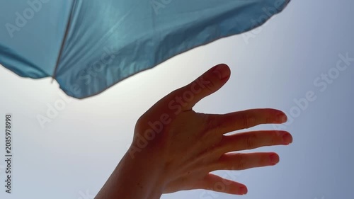 Hand playing with sun rays under blue beach umbrella. 4k