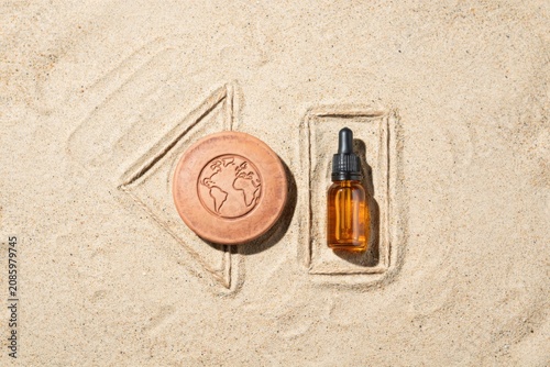 A soap bar and a bottle of oil are placed in the sand.
