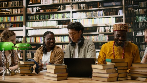 Canvastavla Diverse students discuss classwork during group study around library table with books and green lamps, showing academic collaboration