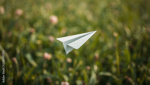 White Paper Airplane Flying Over Green Meadow with Soft Bokeh Background