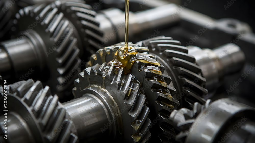 Fototapeta premium Close up of golden oil dripping onto metallic gears and cogs of a heavy machinery transmission system during a routine maintenance procedure