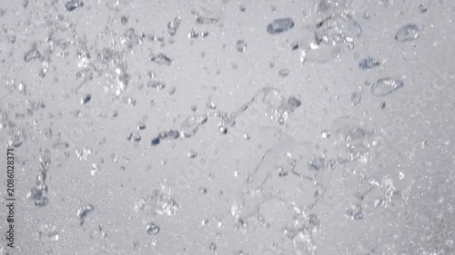 Abstract close-up of falling water droplets creating dynamic splashes and bubbles. Refreshing rainfall or tropical shower background with fluid motion and natural texture
