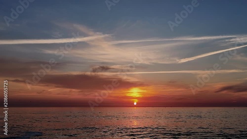 A cinematic time-lapse sequence capturing a vibrant, golden-hour sunset over the Atlantic Ocean at Furadouro Beach in Ovar, Portugal. The footage features the sun slowly descending toward the horizon,