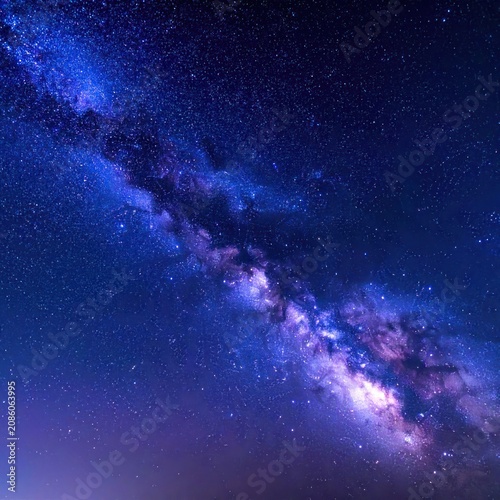 A vibrant band of the Milky Way galaxy stretches across a deep blue, star-filled night sky, with hints of purple and pink in the galactic core.