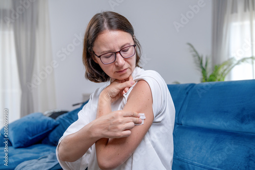 Photography Adult woman with glasses attaching an adhesive glucose monitor patch to her uppe