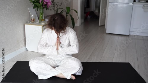 Static Shot Of Woman Meditating With Hands Clasped On Yoga Mat, Lifting Head From Bowed Pose In Home Interior With Kitchen Background.