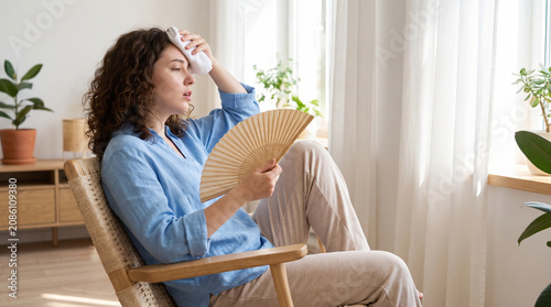 Young woman cooling herself with hand fan in hot living room