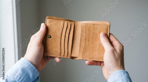 Hands holding an empty brown leather wallet showing multiple card slots and detailed stitched material texture