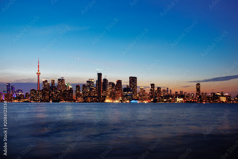 Obraz premium Toronto skyline at dusk with illuminated city lights reflecting on the water, vibrant urban night view. g.