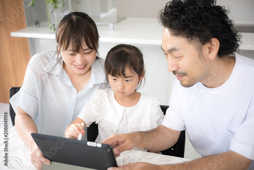 自宅のダイニングやリビングでタブレットを使って家庭学習をする親子3人の家族とデジタル教育のイメージ